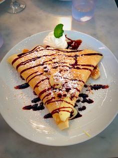 a piece of crepe with chocolate sauce and whipped cream on top sits on a white plate