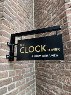 the clock tower sign is mounted on a brick wall with a black metal frame and gold lettering