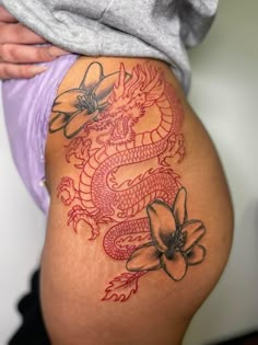 a woman's thigh with a dragon tattoo on the side and flowers around it