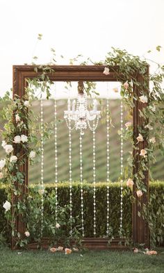 a wooden frame with white flowers and pearls hanging from it is surrounded by greenery