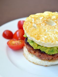 an egg, bacon and avocado sandwich on a white plate with cherry tomatoes