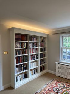 a living room filled with lots of books on top of a white book shelf next to a window