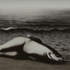 a black and white photo of a woman laying on the beach next to the ocean