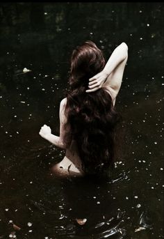 a woman in the water with her back turned to the camera, holding her hands behind her head