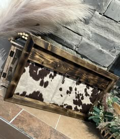 a cow print rug in a wooden box on the ground next to a plant and brick wall