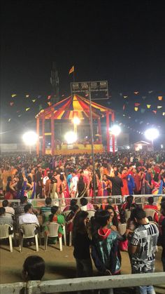 a large group of people standing around in front of a circus tent at night time