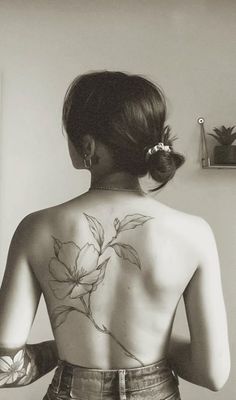 a woman with tattoos on her back standing next to a wall