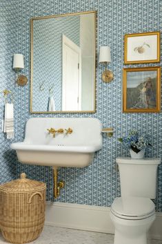 a white toilet sitting next to a sink in a bathroom under a mirror and pictures on the wall