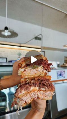 a person holding up a large sandwich with meat and cheese on it in front of a counter