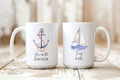 two coffee mugs sitting on top of a wooden table with anchors and an anchor