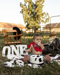 a baby sitting in the grass eating cake next to a rocking chair and one sign