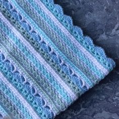 a blue and white crocheted blanket sitting on top of a stone floor next to a cup