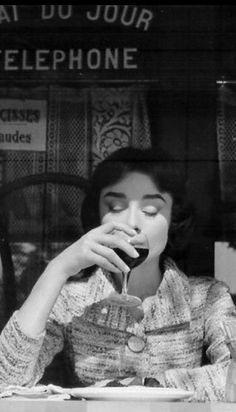 a woman sitting at a table eating food and drinking from a cup in front of her