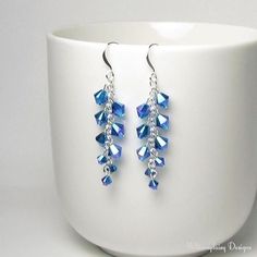 a pair of blue crystal earrings sitting on top of a white cup