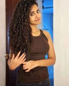 a woman with long curly hair standing in front of a door and looking at the camera