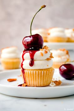 a cupcake with white frosting and cherries on top sitting on a plate