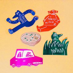 four different colored paper cut outs on top of a yellow surface with cars and trees in the background