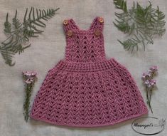 a pink crocheted dress sitting on top of a table next to some flowers