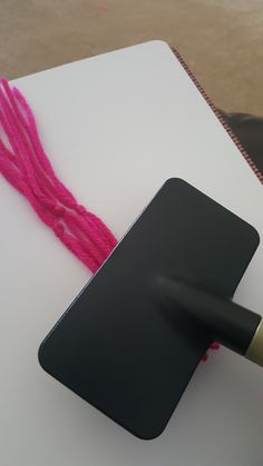 a person holding a knife over a piece of paper with pink thread on it and another item in the background