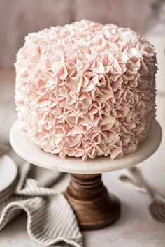 a close up of a cake with pink icing on a white plate next to silverware