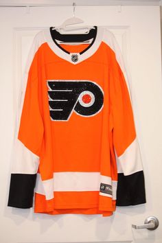 an orange hockey jersey hanging on a door with the philadelphia flyers logo in black and white