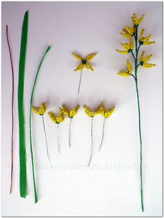 yellow flowers and green stems are arranged on a white surface with long grass stalks in the foreground