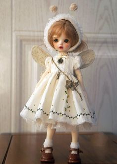 a doll is wearing a white dress and bonnet on top of a wooden table with a door in the background