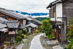 a narrow street with wooden buildings and mountains in the background, surrounded by greenery