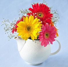 a white pitcher filled with lots of colorful flowers