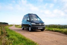 a black van driving down a dirt road next to grass and water on a sunny day