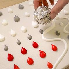 a person is placing something on top of a board game with red and silver drops