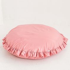 a pink round pillow with ruffled edges on a white background in front of a wall