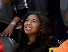 a young woman sitting in the stands at a basketball game, looking up and smiling