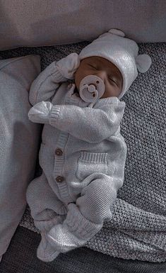 a baby in a white outfit laying on top of a bed next to a pillow