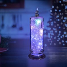 a lit candle sitting on top of a table next to a christmas tree in the background