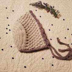 a crocheted hat laying on top of a bed next to a lavender sprig