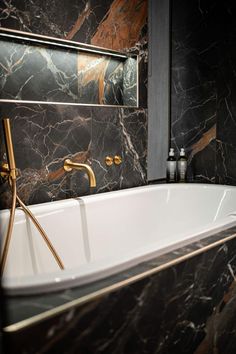 a bathtub in a bathroom with black marble walls and flooring, along with brass faucets