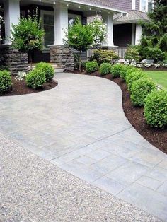 a driveway with landscaping in front of it and bushes around the walkways on both sides