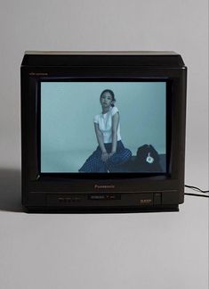 a woman sitting on the floor in front of an old tv with her legs crossed