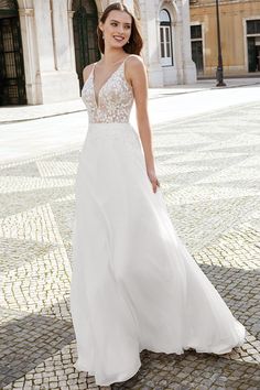 a woman in a white wedding dress standing on a cobblestone street with an old building in the background