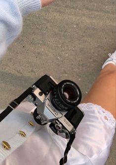 a person holding a camera in their right hand while wearing white pants and laces