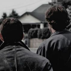 two men standing in front of a house looking at the back of another man's head