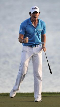 a man holding a golf club in his right hand and yelling on the green with water in the background