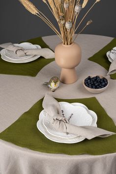 a table topped with plates and bowls filled with blueberries next to a vase full of dry grass