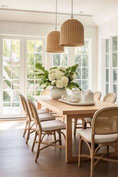 a dining room table with chairs and vases on it's centerpiece in front of large windows