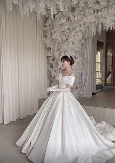 a woman in a white wedding dress standing next to a flower covered wall with flowers hanging from it