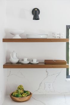 two shelves with bowls and plates on them in a room that has white marble walls