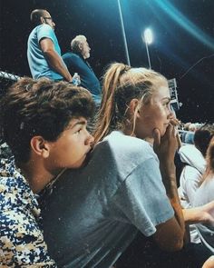 several people sitting in the stands at a baseball game and one person is holding his hand up to his mouth