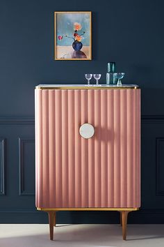 a pink cabinet with two wine glasses on top and a painting above it in a blue room