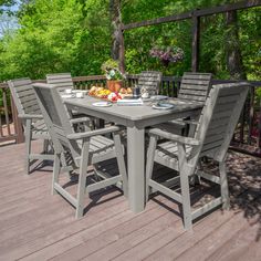 an outdoor table and chairs on a deck with flowers in vases, fruit and water